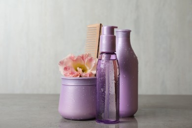 Different hair products, flower and wooden comb on grey table