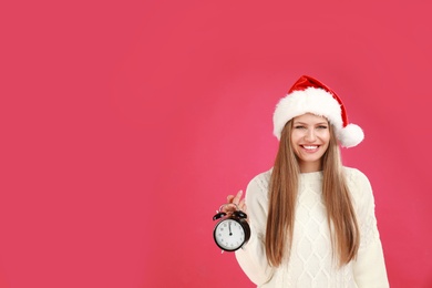 Photo of Happy young woman in Santa hat with alarm clock on pink background, space for text. Christmas time