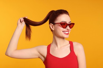 Photo of Happy woman with red dyed hair and sunglasses on orange background