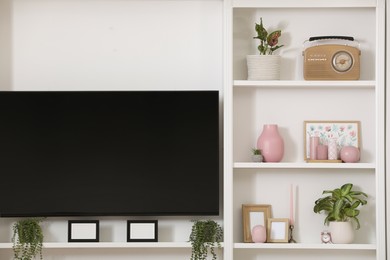 Photo of TV set and stylish shelves with decorative elements and houseplants near white wall. Interior design