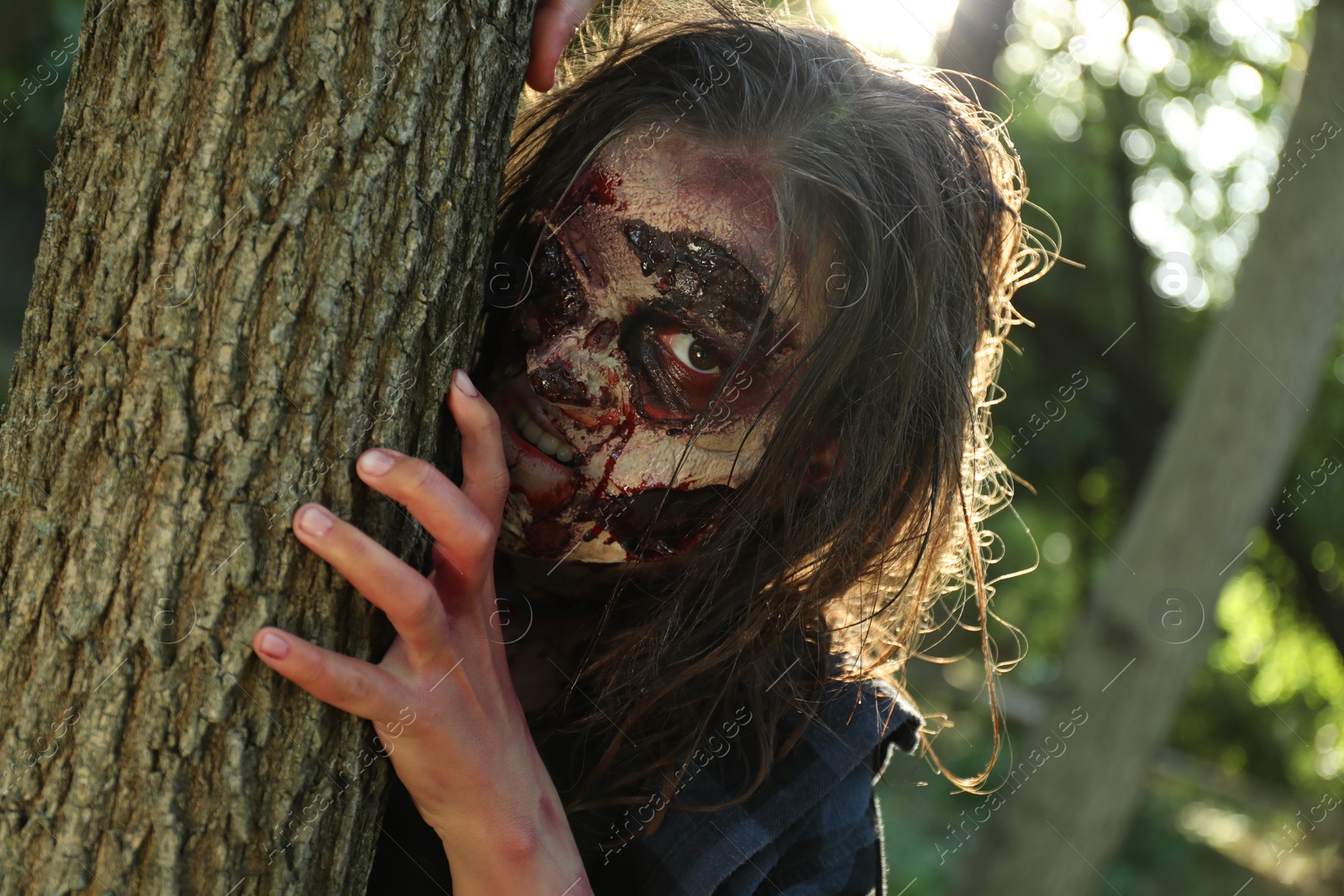 Photo of Scary zombie near tree outdoors. Halloween monster