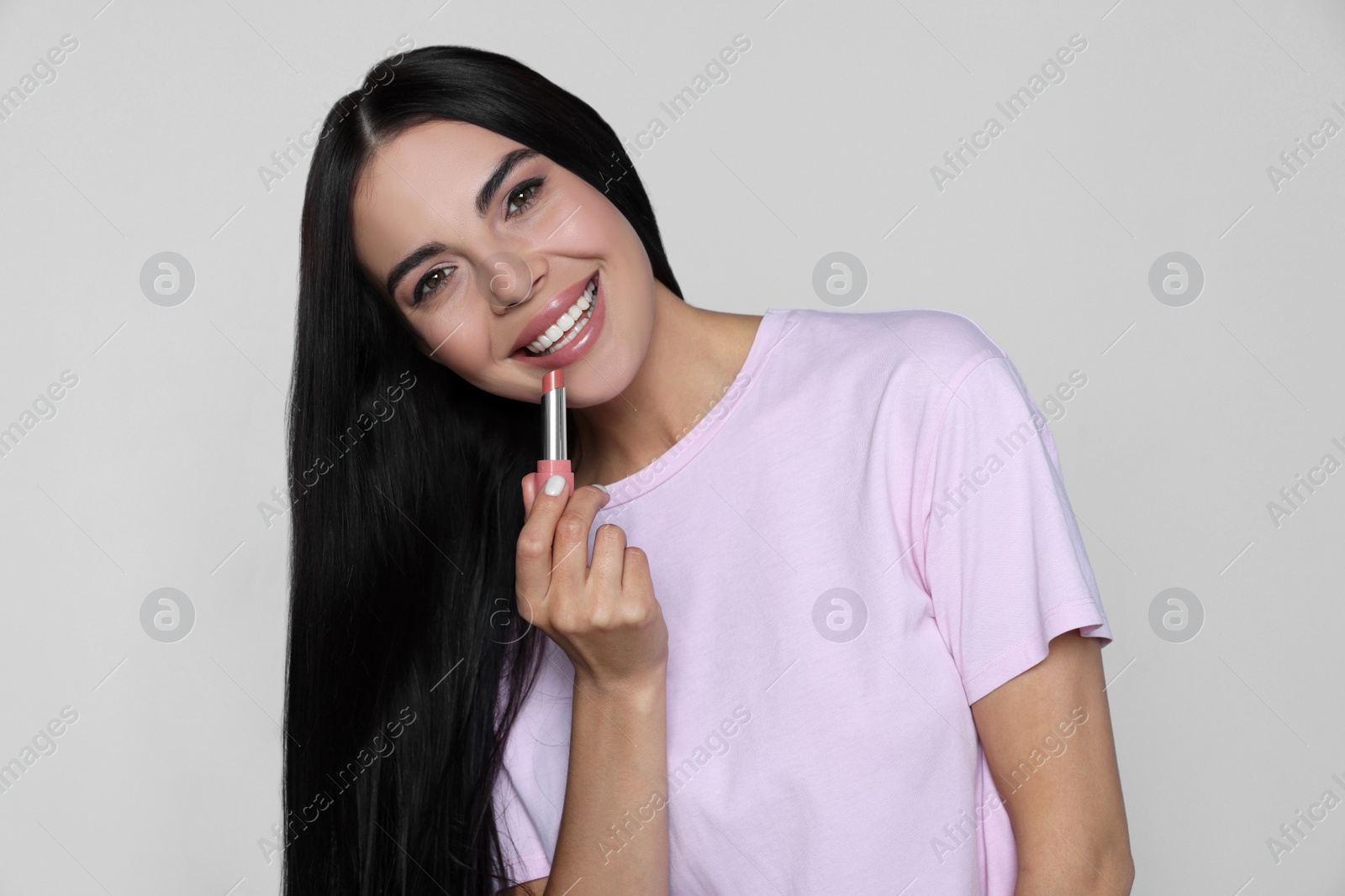 Photo of Young woman with beautiful makeup holding nude lipstick on light gray background
