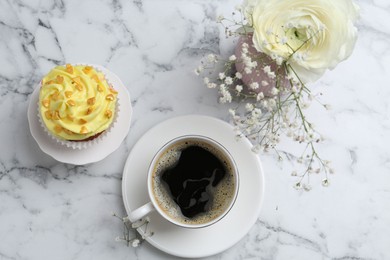 Photo of Delicious cupcake with yellow cream, coffee and flowers on white marble table, flat lay