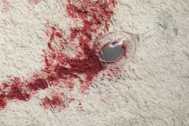 Photo of Overturned glass and spilled red wine on white carpet, top view