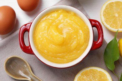 Photo of Delicious lemon curd in bowl, ingredients and spoon on table, flat lay
