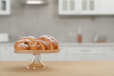 Stand with delicious croissants on table in kitchen, space for text