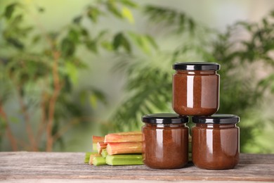Photo of Jars of tasty rhubarb jam and stalks on wooden table. Space for text