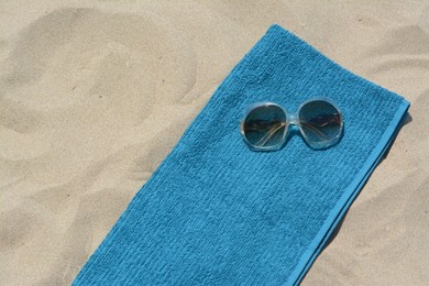 Soft blue beach towel with sunglasses on sand, top view. Space for text