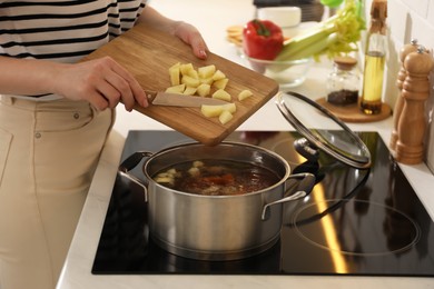 Photo of Woman putting potato into pot to make bouillon in kitchen, closeup. Homemade recipe