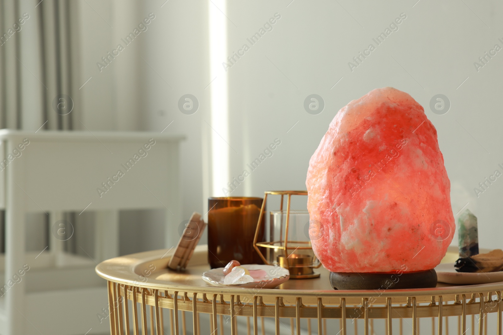 Photo of Himalayan salt lamp, candles and crystals on golden table indoors, space for text