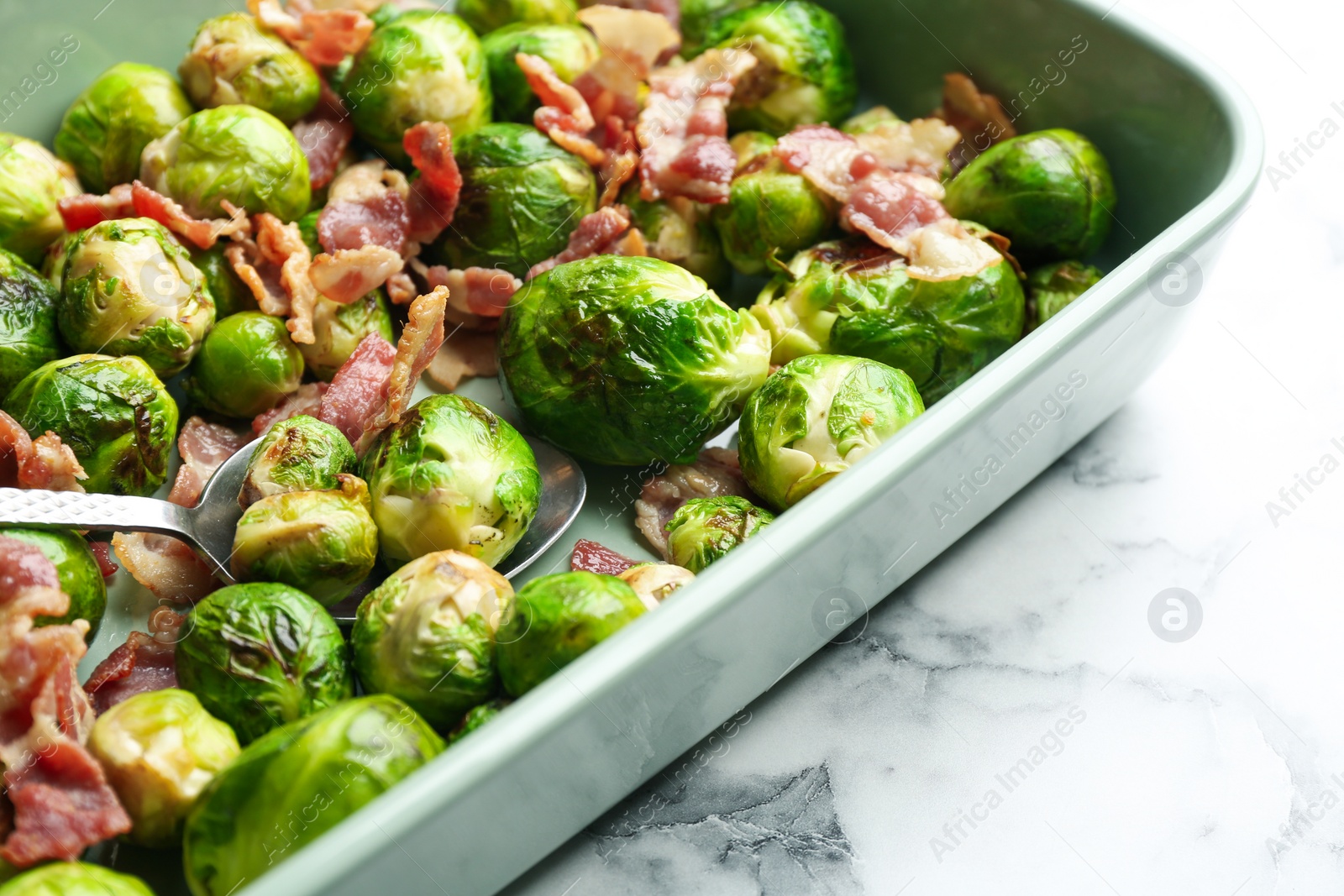 Photo of Delicious Brussels sprouts with bacon on white marble table, closeup