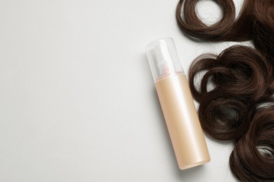 Photo of Spray bottle with thermal protection and lock of brown hair on light grey background, flat lay. Space for text