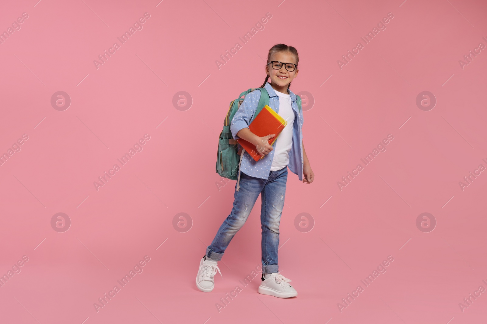 Photo of Happy schoolgirl in glasses with backpack and books on pink background