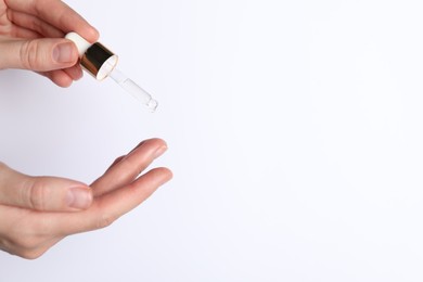 Photo of Woman applying cosmetic serum onto fingers on white background, closeup. Space for text