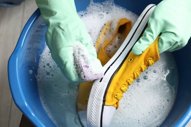 Woman with gloves and sponge cleaning stylish sneakers in wash basin, top view