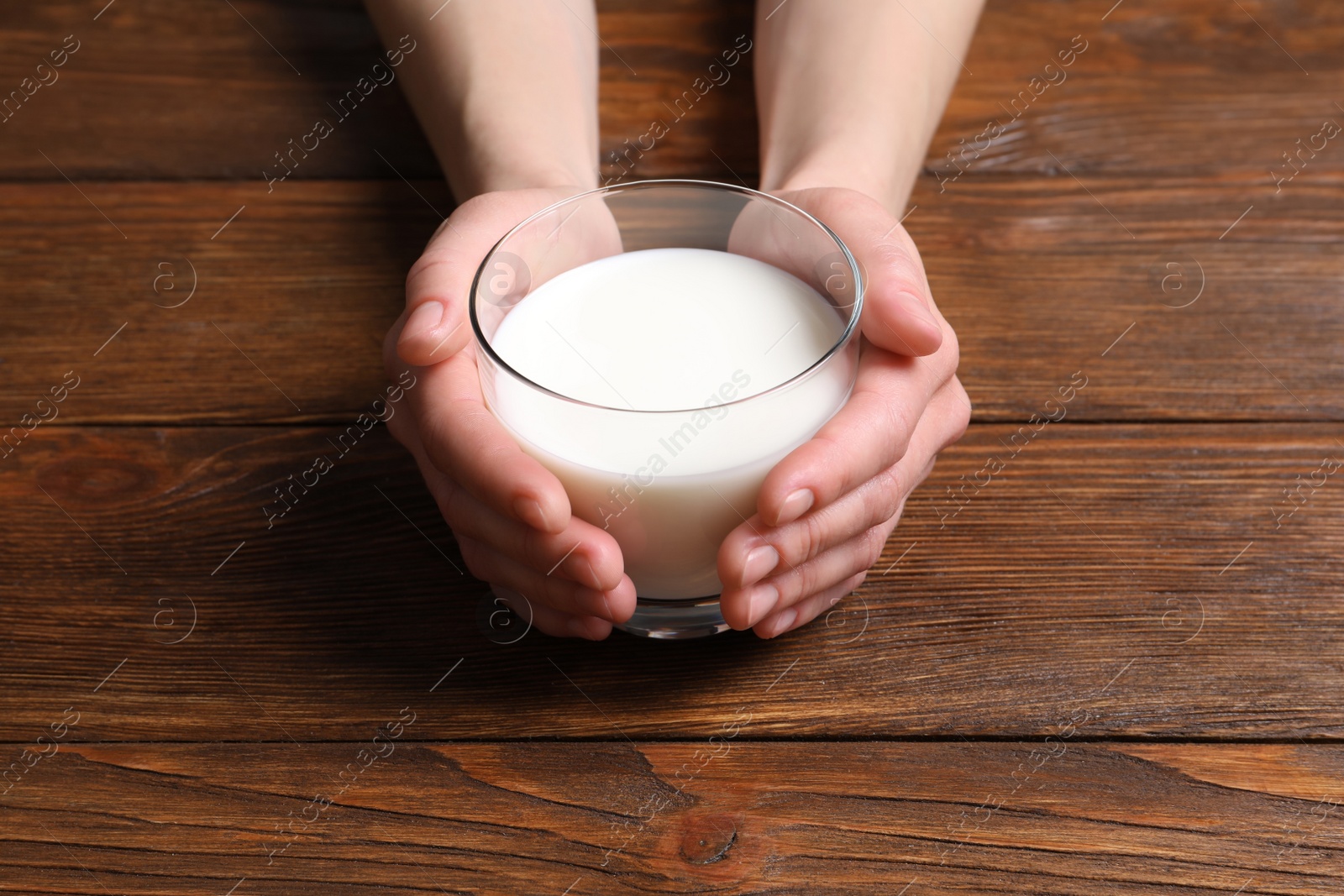 Photo of Woman holding glass of milk at wooden table, closeup