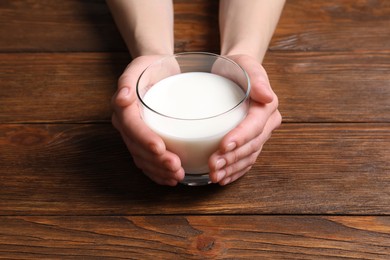 Photo of Woman holding glass of milk at wooden table, closeup