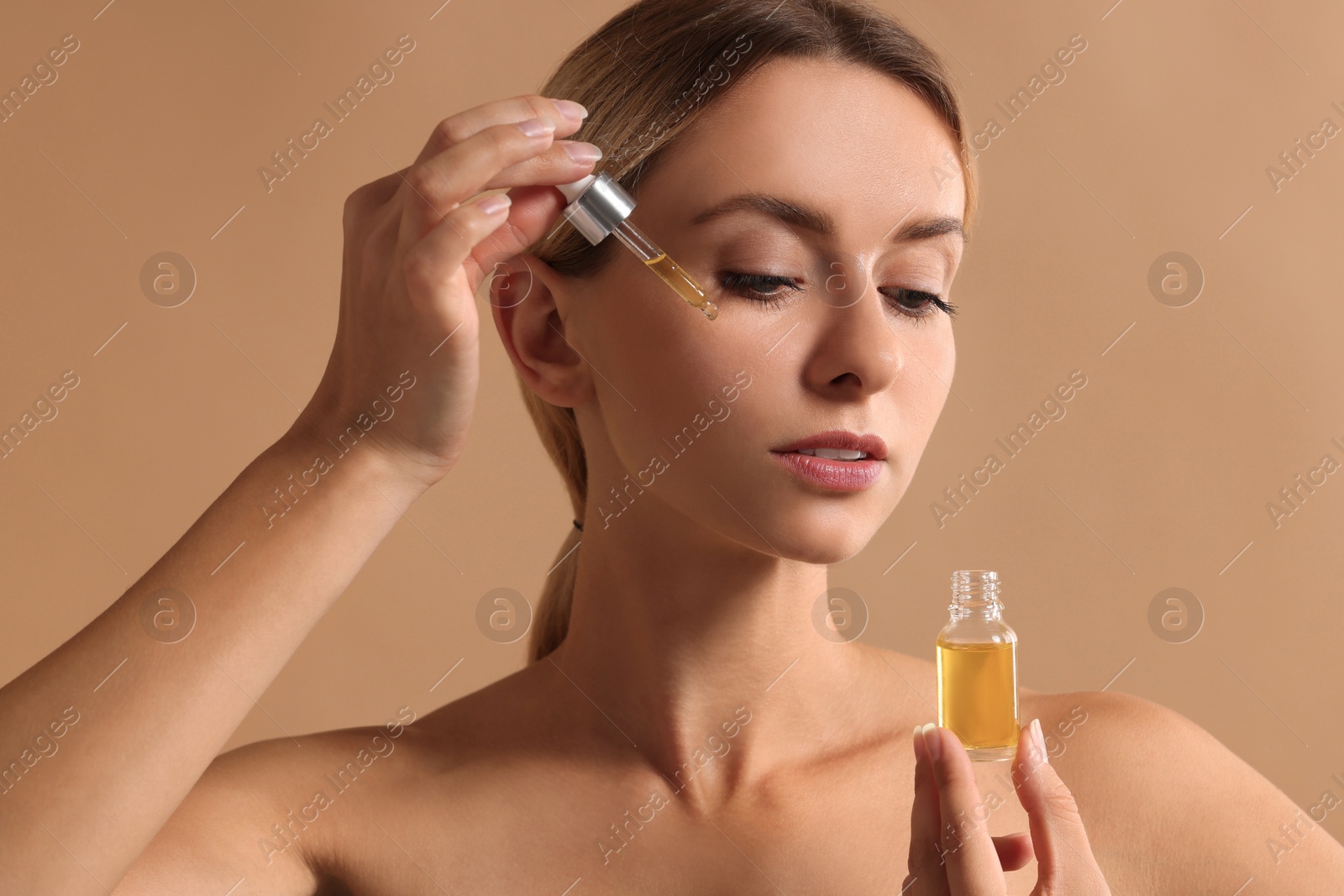 Photo of Beautiful woman applying cosmetic serum onto her face on beige background