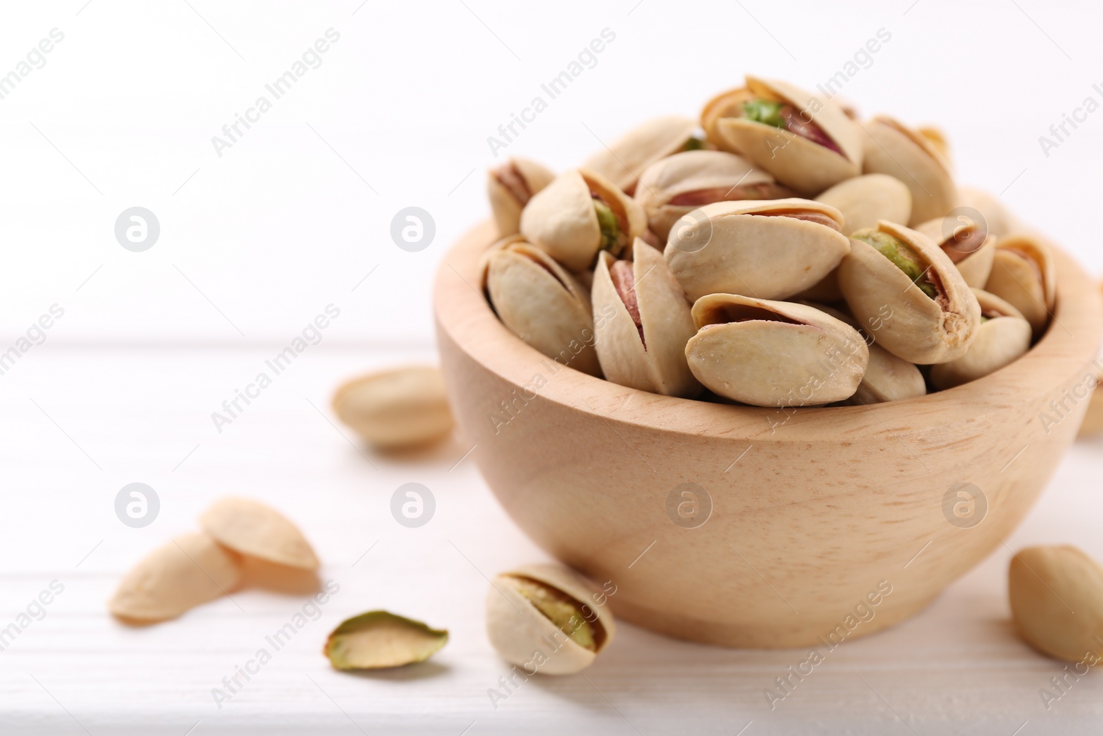 Photo of Tasty pistachios in bowl on white wooden table, closeup. Space for text