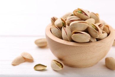 Tasty pistachios in bowl on white wooden table, closeup. Space for text