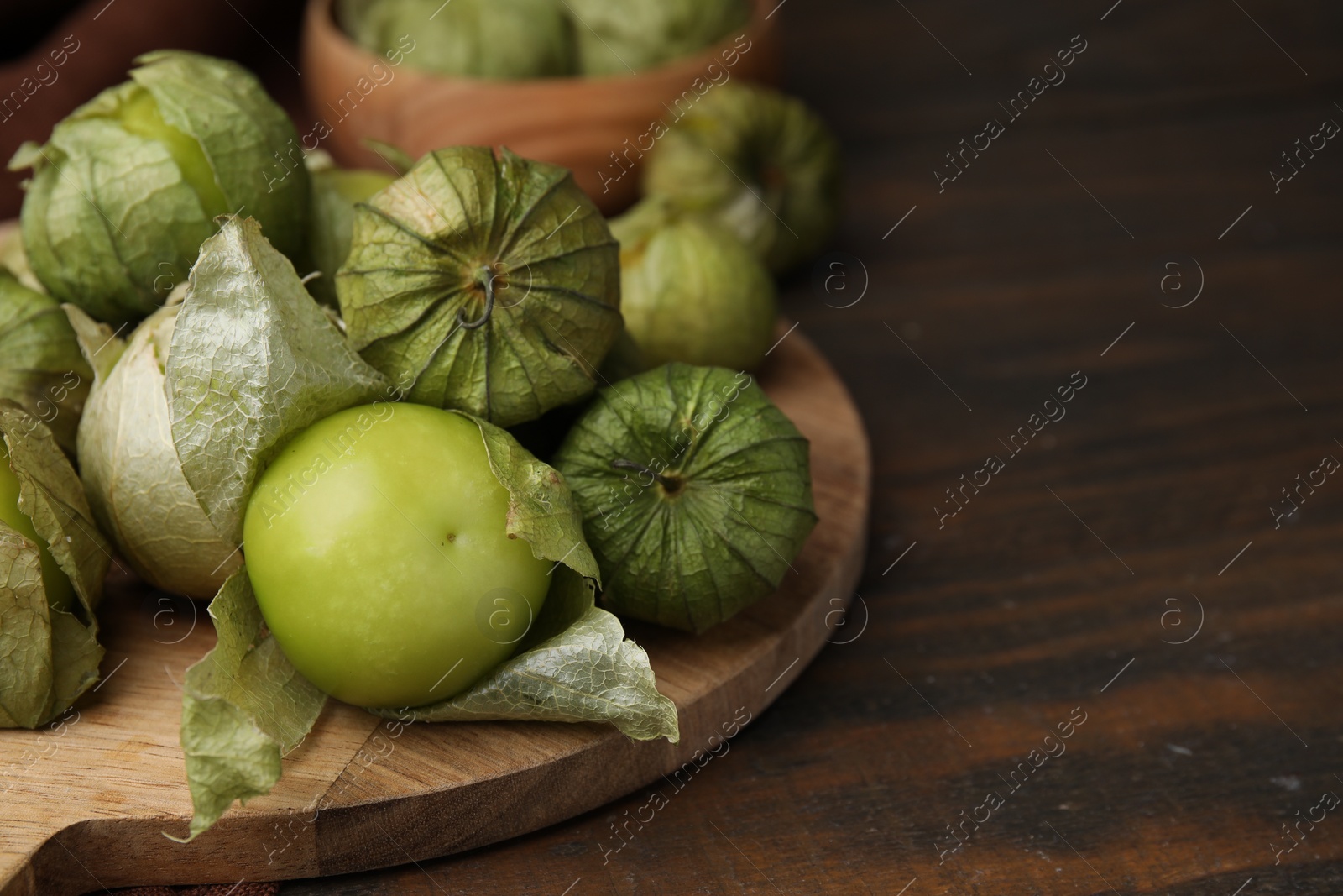 Photo of Fresh green tomatillos with husk on wooden table, closeup. Space for text