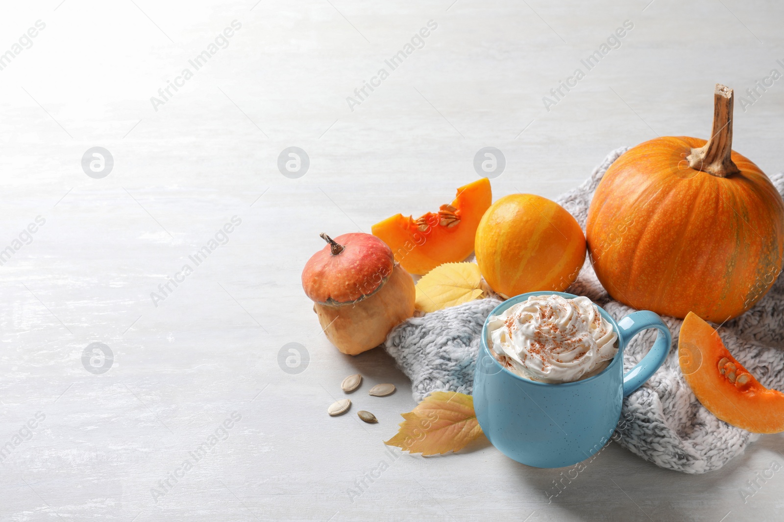 Photo of Cup with pumpkin spice latte, autumn decor and space for text on light table