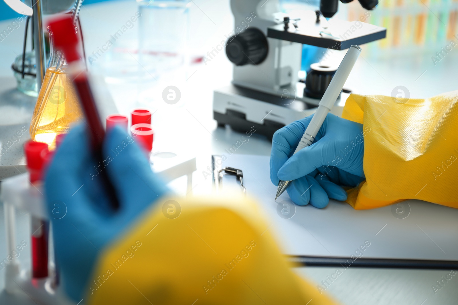 Photo of Scientist in chemical protective suit working with blood samples at table, closeup. Virus research