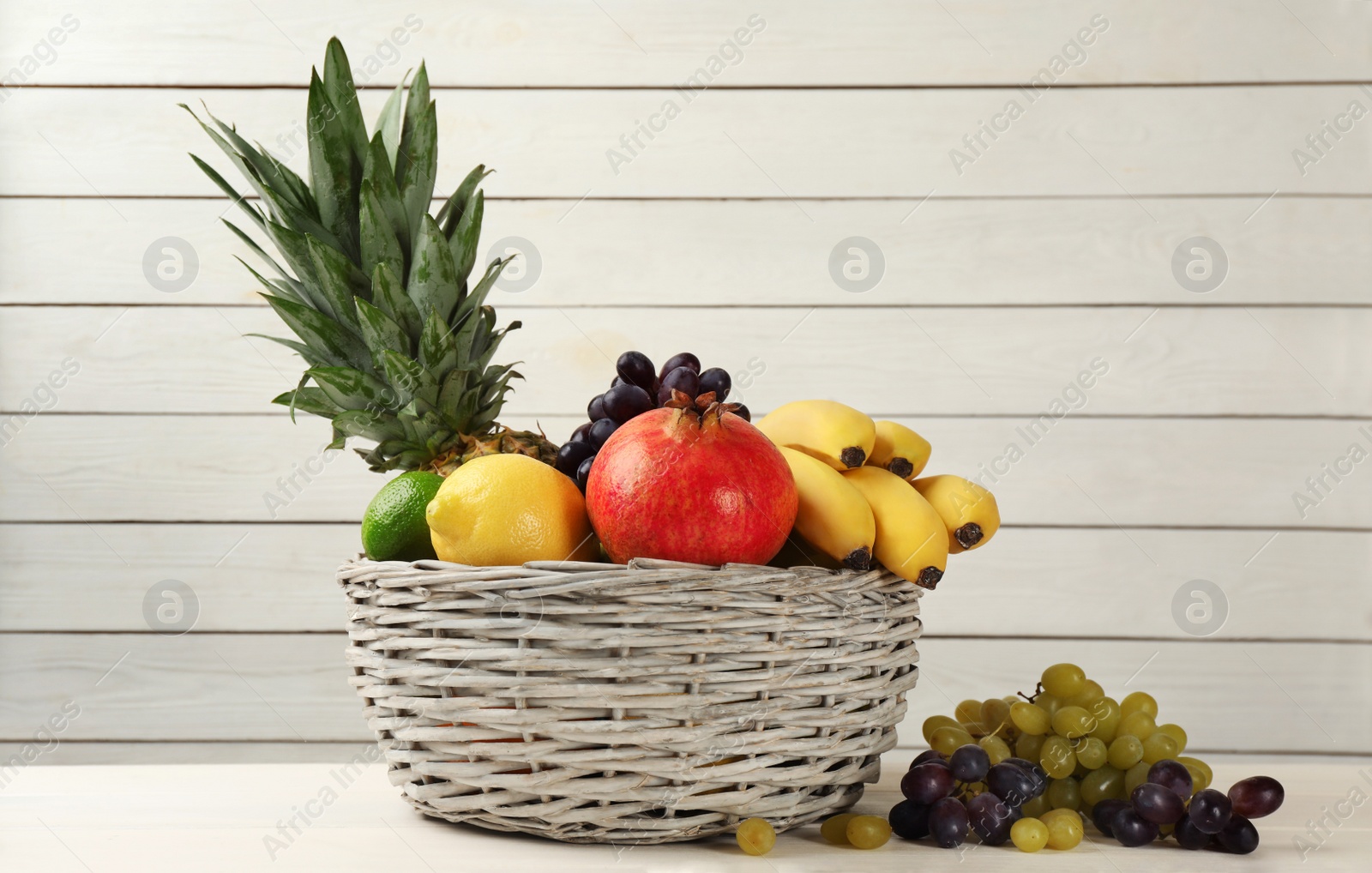 Photo of Wicker bowl with different ripe fruits on white wooden table