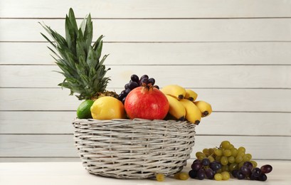 Wicker bowl with different ripe fruits on white wooden table