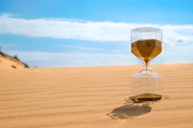 Photo of Hourglass with flowing sand in desert on sunny day. Space for text