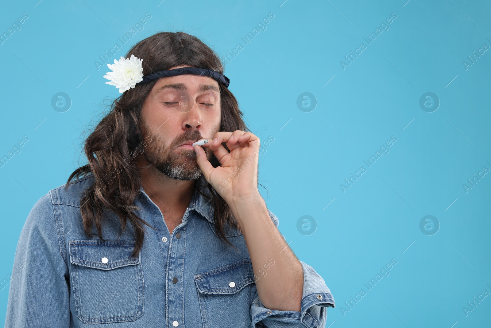 Photo of Stylish hippie man smoking cigarette on light blue background, space for text