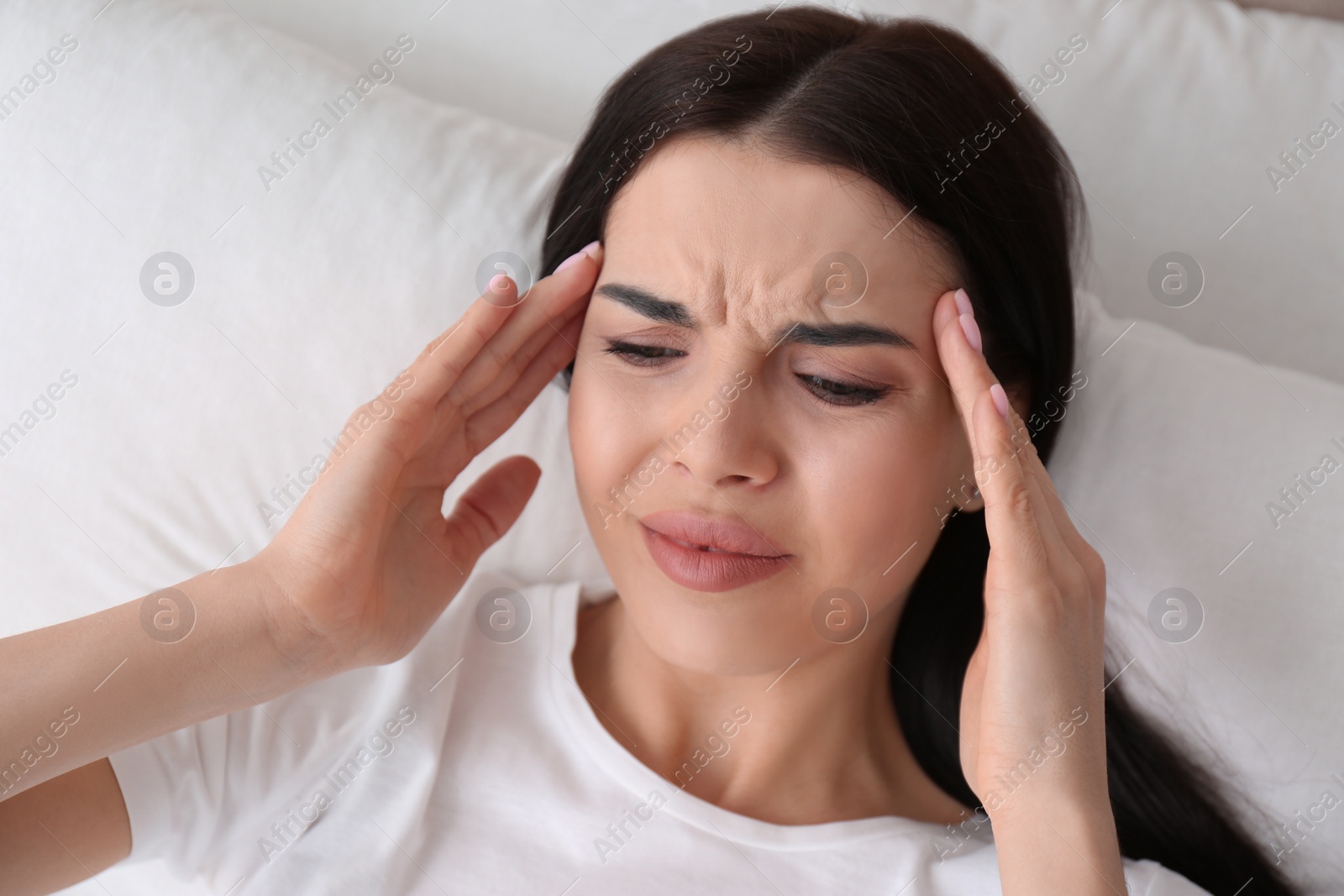 Photo of Young woman suffering from migraine in bed, above view