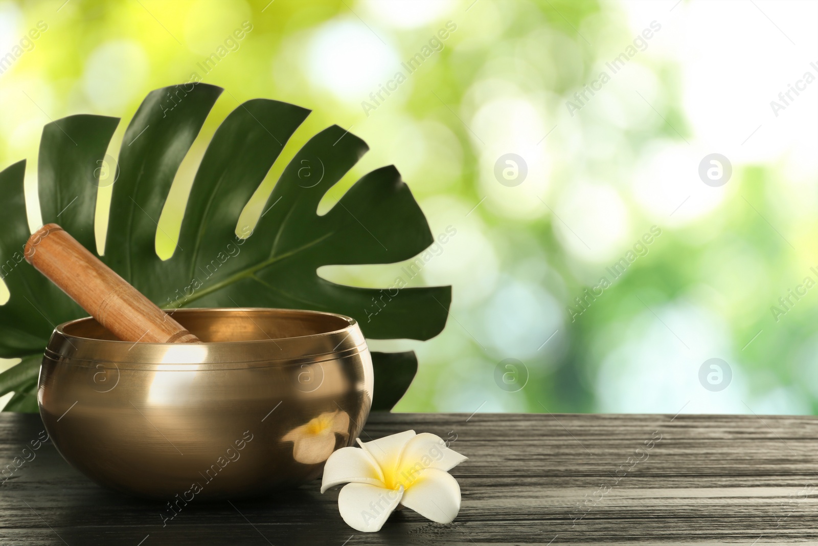 Image of Golden singing bowl, mallet, green leaf and flower on wooden table outdoors, space for text