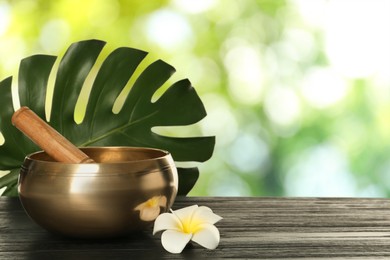 Image of Golden singing bowl, mallet, green leaf and flower on wooden table outdoors, space for text