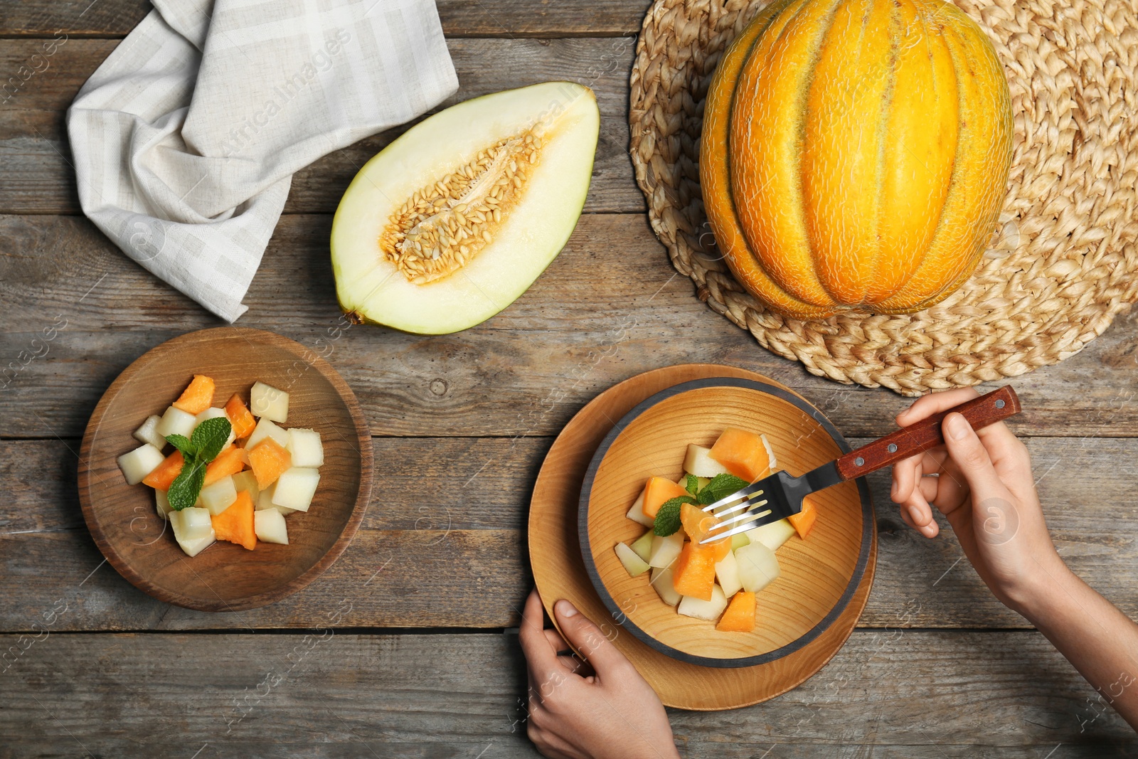 Photo of Woman eating salad with assorted melons at wooden table, top view