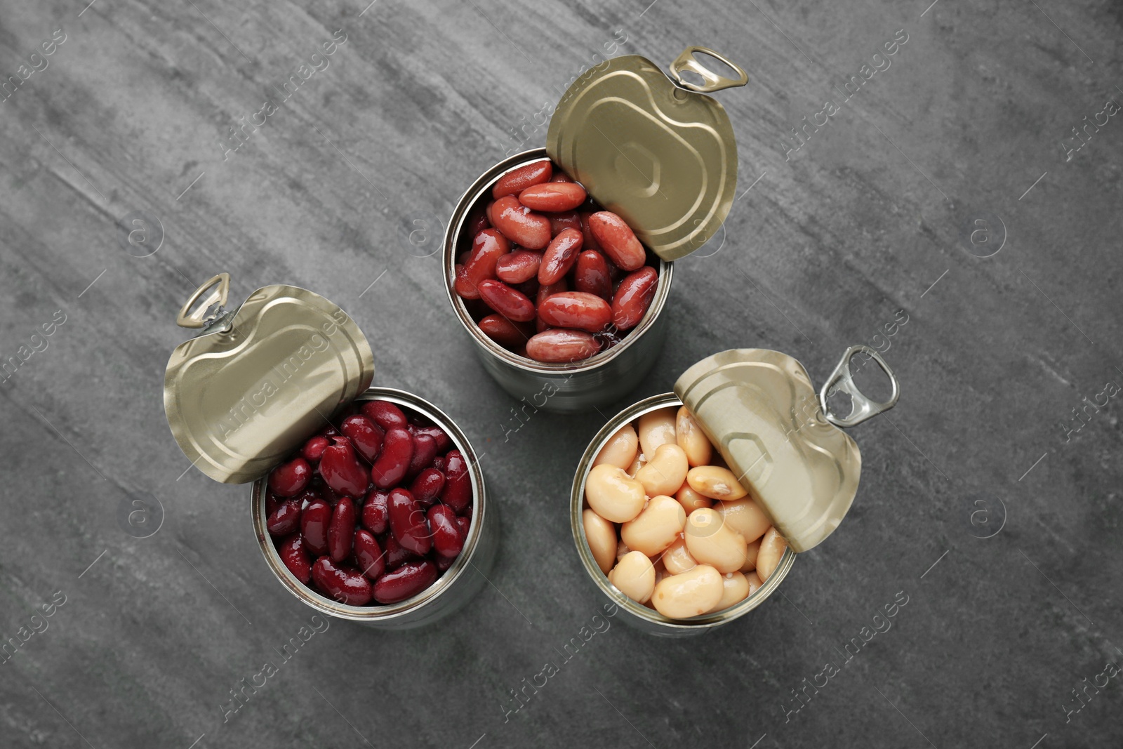 Photo of Tin cans with different canned kidney beans on grey table, flat lay