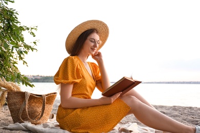 Photo of Young woman reading book on sandy beach near sea