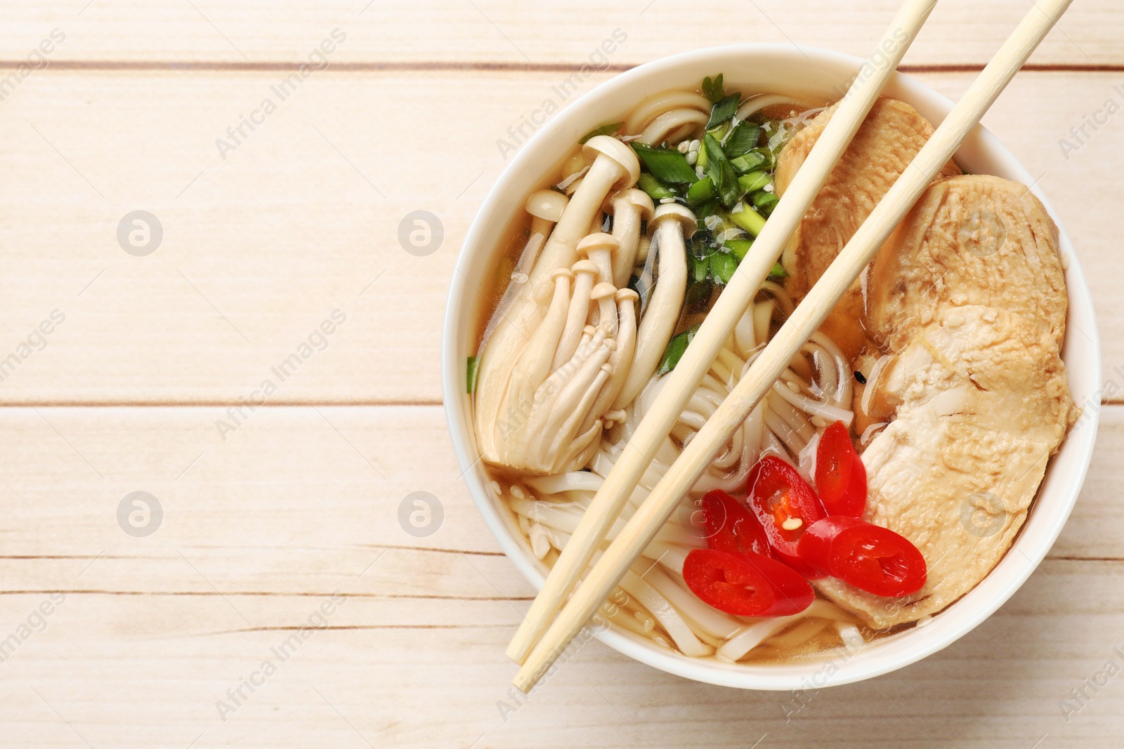 Photo of Delicious ramen with meat and mushrooms in bowl and chopsticks on white wooden table, top view. Space for text