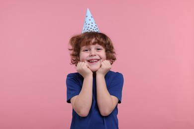 Happy little boy in party hat on pink background