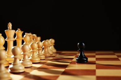 Photo of Black pawn in front of white pieces on wooden board against dark background. Competition concept