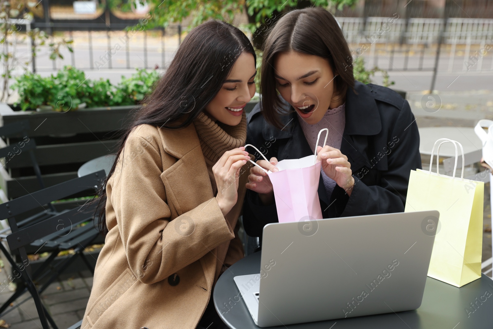 Photo of Special Promotion. Emotional young women with shopping bags using laptop in outdoor cafe