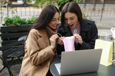 Photo of Special Promotion. Emotional young women with shopping bags using laptop in outdoor cafe
