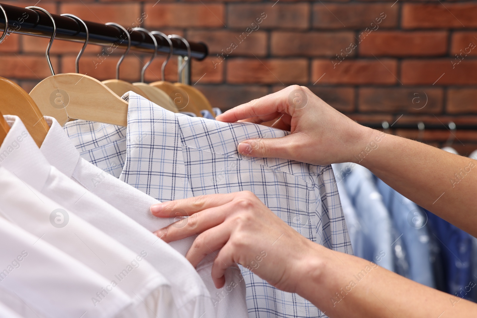 Photo of Dry-cleaning service. Woman taking shirt from rack against brick wall, closeup