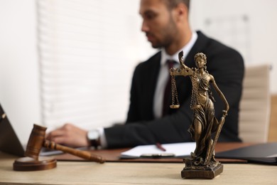Lawyer working with laptop at table in office, focus on statue of Lady Justice