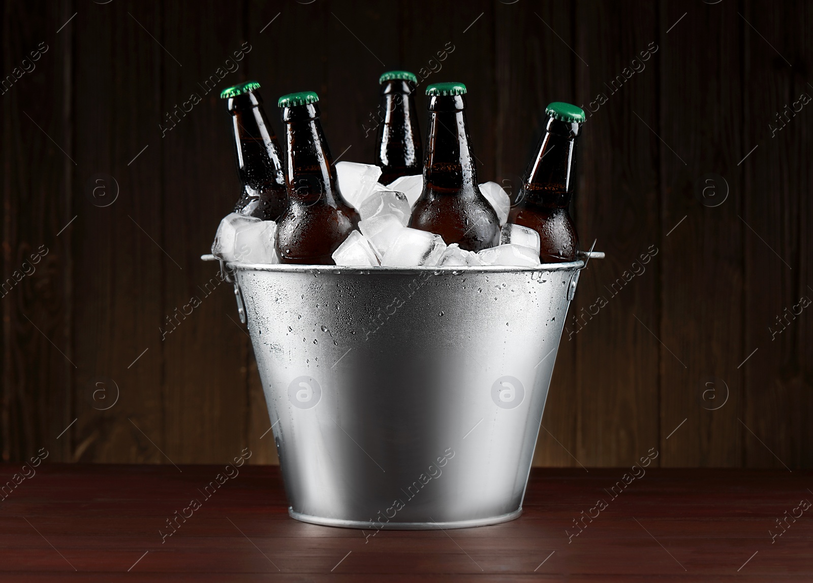 Photo of Metal bucket with bottles of beer and ice cubes on wooden table