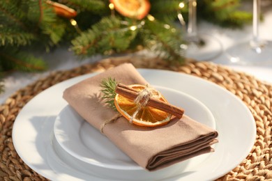 Festive place setting with beautiful dishware, fabric napkin and dried orange slice for Christmas dinner on white table, closeup