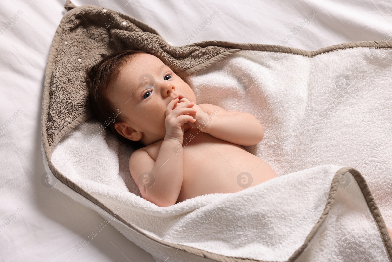 Photo of Cute little baby in hooded towel after bathing on bed, top view