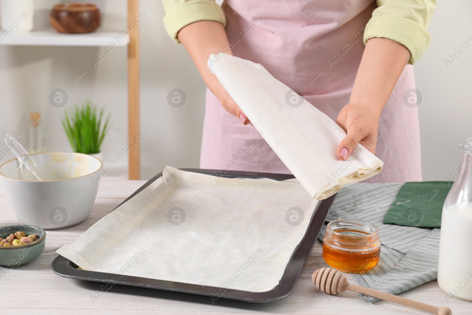 Photo of Woman making delicious baklava at white wooden table, closeup