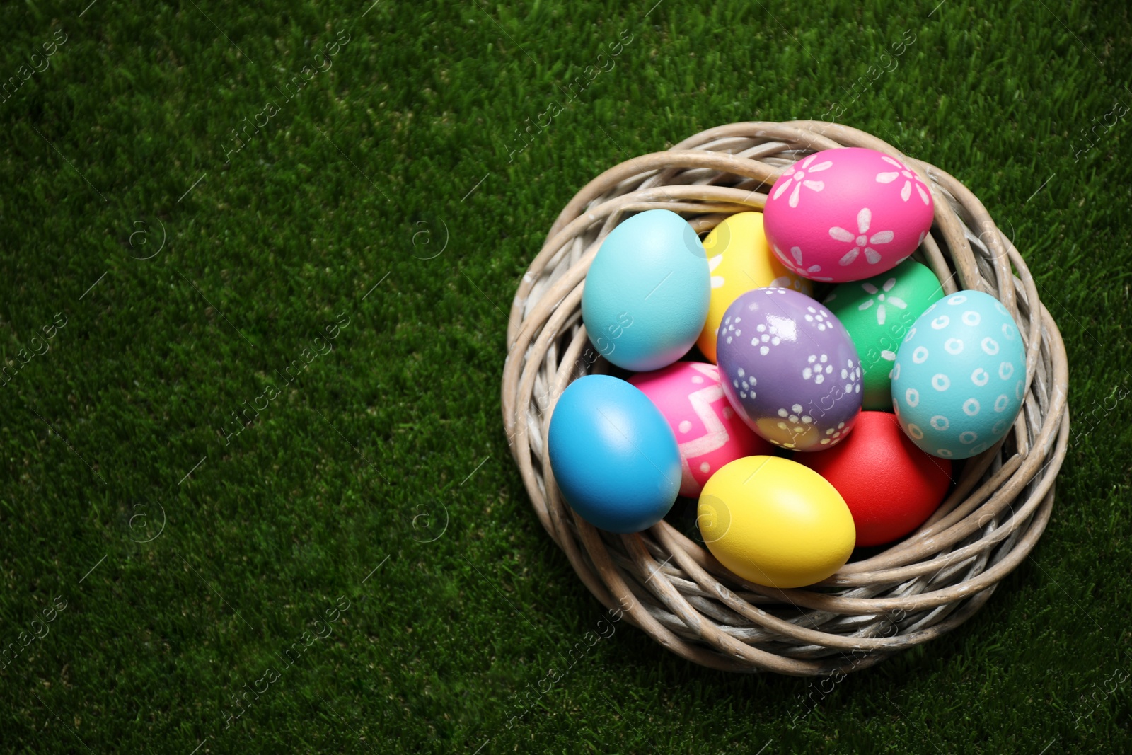 Photo of Colorful Easter eggs in decorative nest on green grass, top view. Space for text