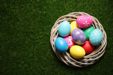 Photo of Colorful Easter eggs in decorative nest on green grass, top view. Space for text